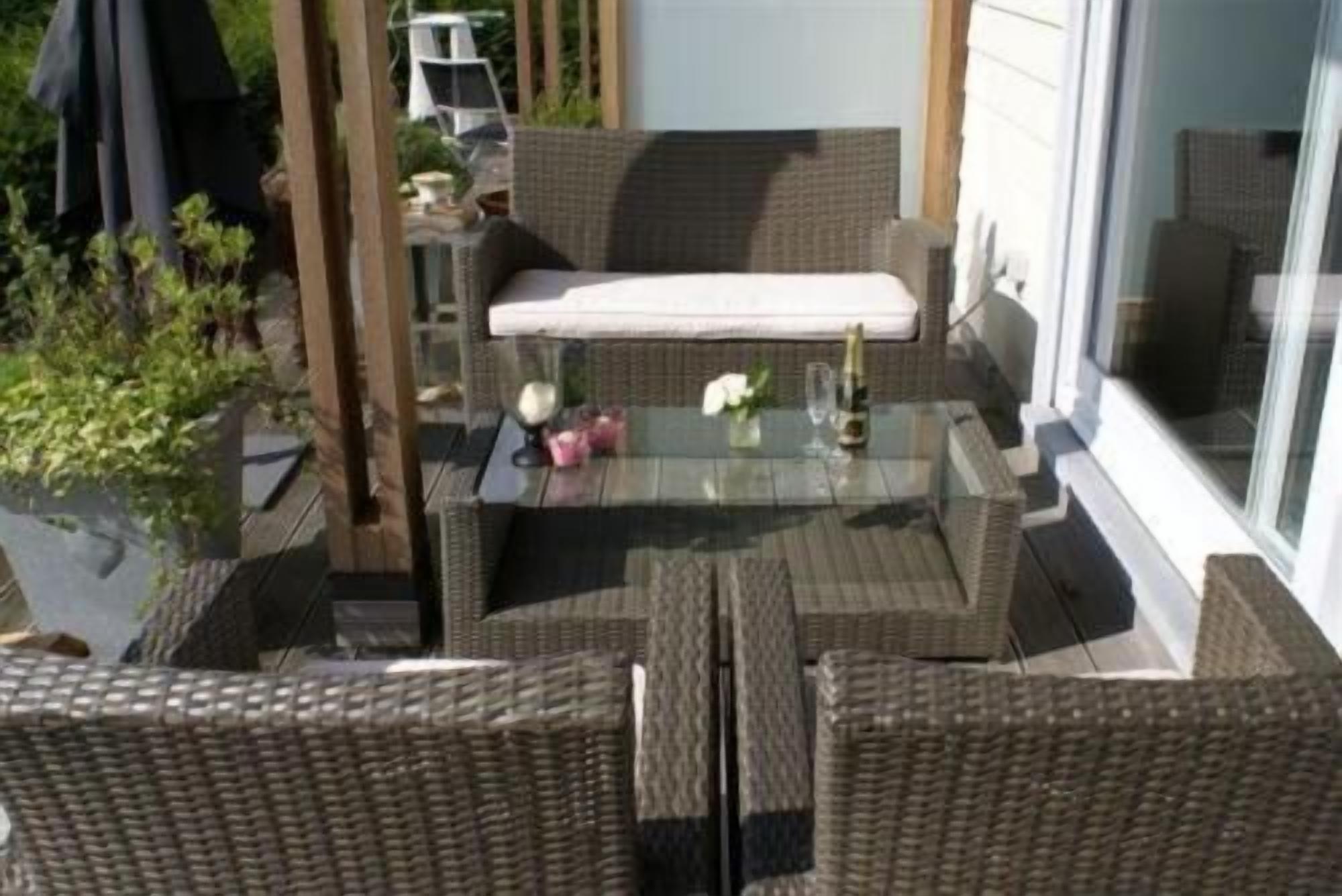 Un espace de détente extérieur aménagé avec des meubles en osier, comprenant une table en verre, un banc et un pot de fleurs.