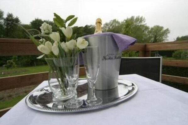 A table with a metal tray, a glass vase with white flowers, and a champagne bucket.