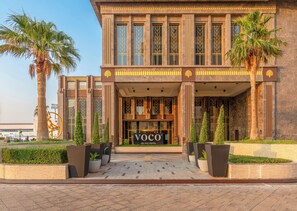 Un hotel modern amb una entrada imponent, palmeres i un logotip.