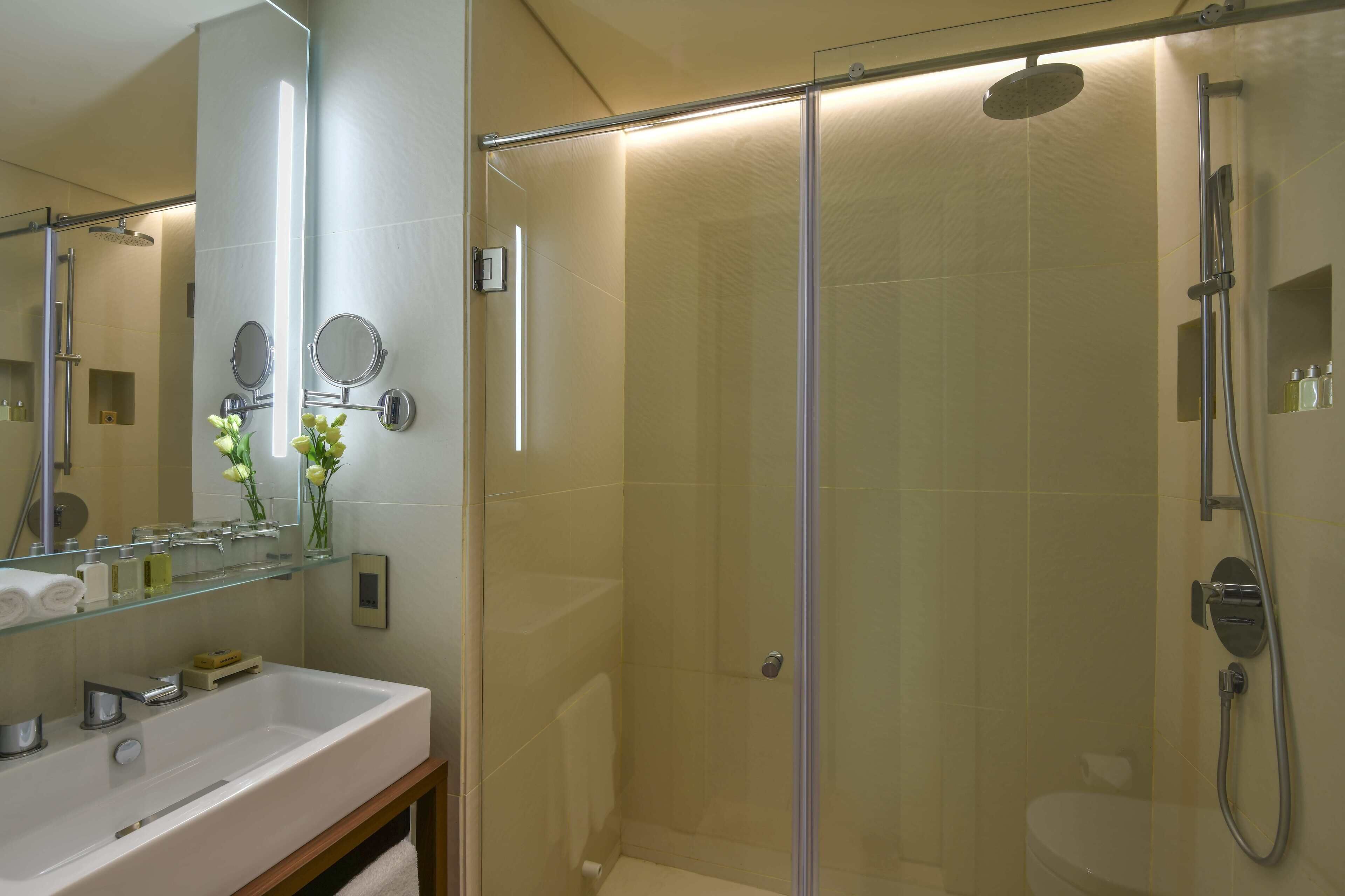 A modern bathroom with a glass-enclosed shower, a large mirror, and a vanity with toiletries.