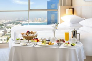 A breakfast table with various dishes, a pitcher of orange juice, and a view of a cityscape through large windows. - voco Doha West Bay Suites by IHG (Doha)