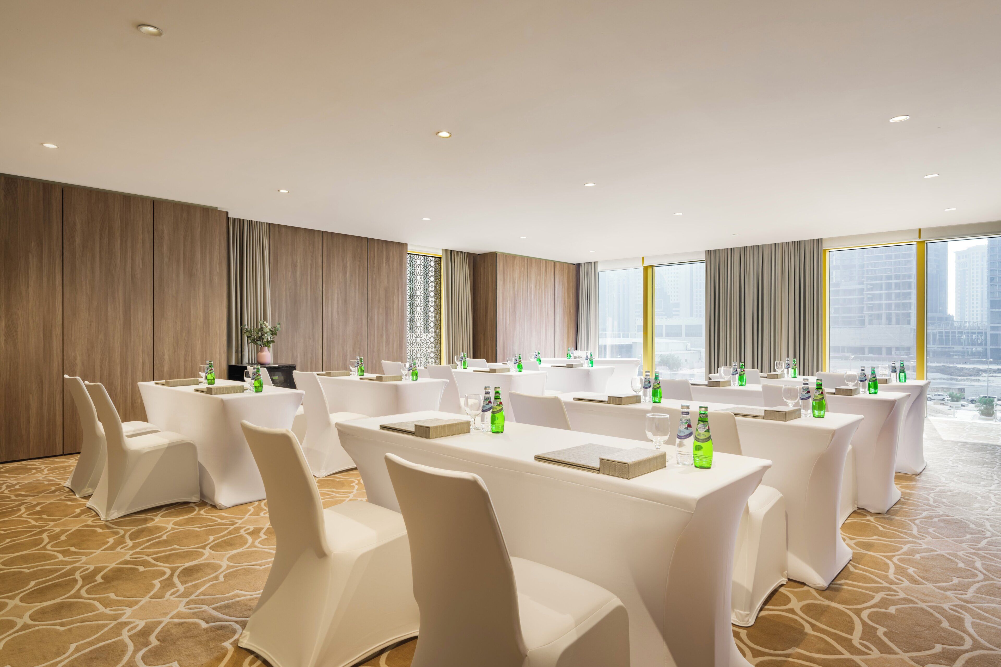 Un salón de conferencias con mesas y sillas blancas, ventanas amplias y vistas a la ciudad.