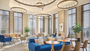 Un moderno vestíbulo de hotel con un sofá azul, mesas redondas y una planta grande.