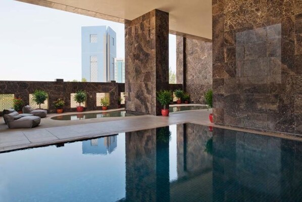 Zona d'una piscina interior moderna, amb parets de marbre i una piscina cristal·lina, envoltada de plantes en testos i zones d'estar.