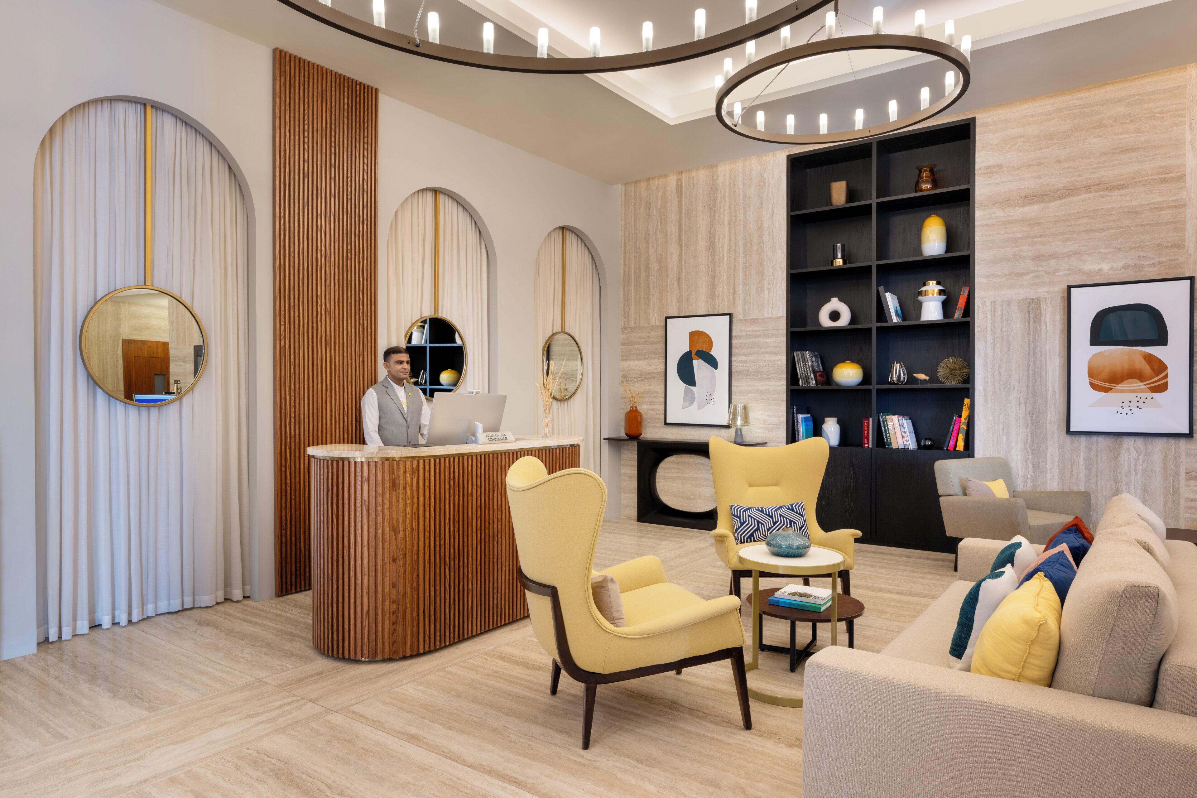 Ett modernt receptionsområde med en receptionsdisk i trä, en sittgrupp med en gul fåtölj och en bokhylla fylld med dekorativa föremål.