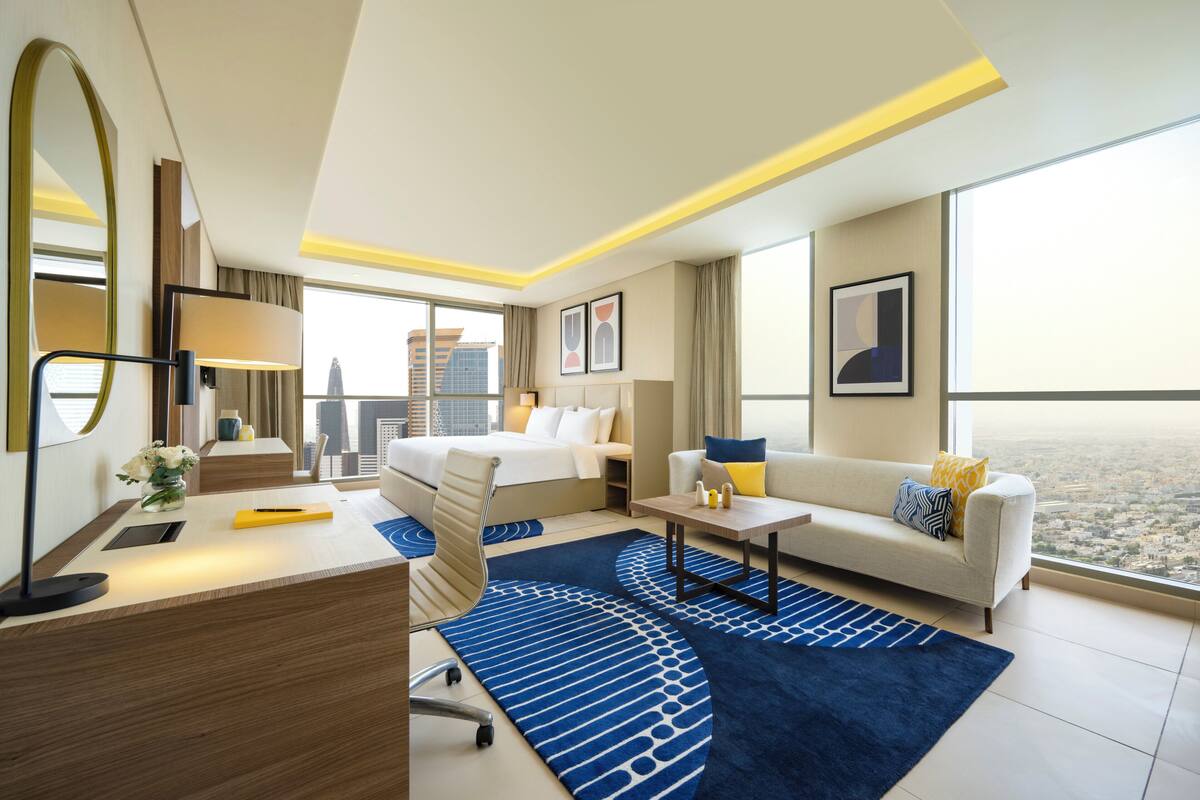 Et moderne hotelværelse med seng, sofa, skrivebord og stort vindue med udsigt over byen.