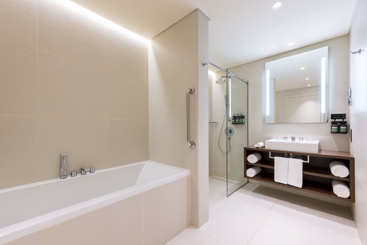 A modern bathroom with a bathtub, glass shower enclosure, and a vanity with a mirror and towel rack.