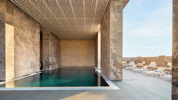 Una piscina infinita en la azotea con vistas al horizonte de la ciudad, rodeada de muros de piedra y sillones de descanso.