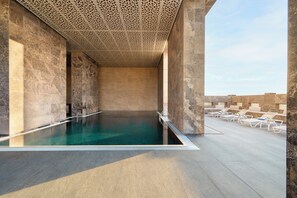 A rooftop infinity pool with a view of the city skyline, surrounded by stone walls and lounge chairs. - voco Doha West Bay Suites by IHG (Doha)