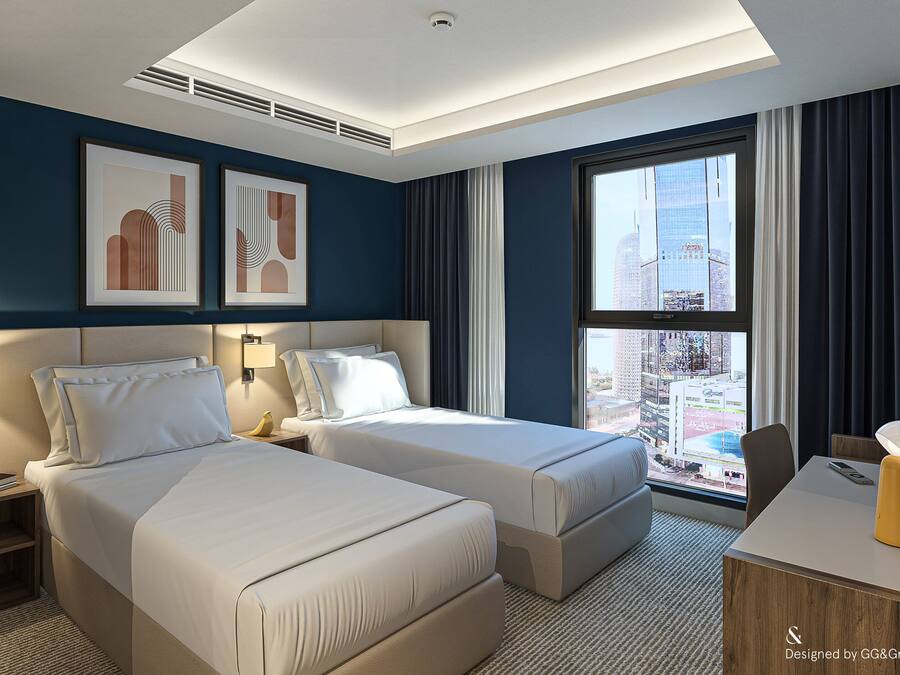 Habitación de hotel con dos camas, un escritorio, una silla, un ventanal con vista a la ciudad y obras de arte en la pared.