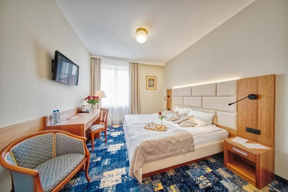 Una habitación de hotel con cama, escritorio, silla, televisor y mesita de noche.
