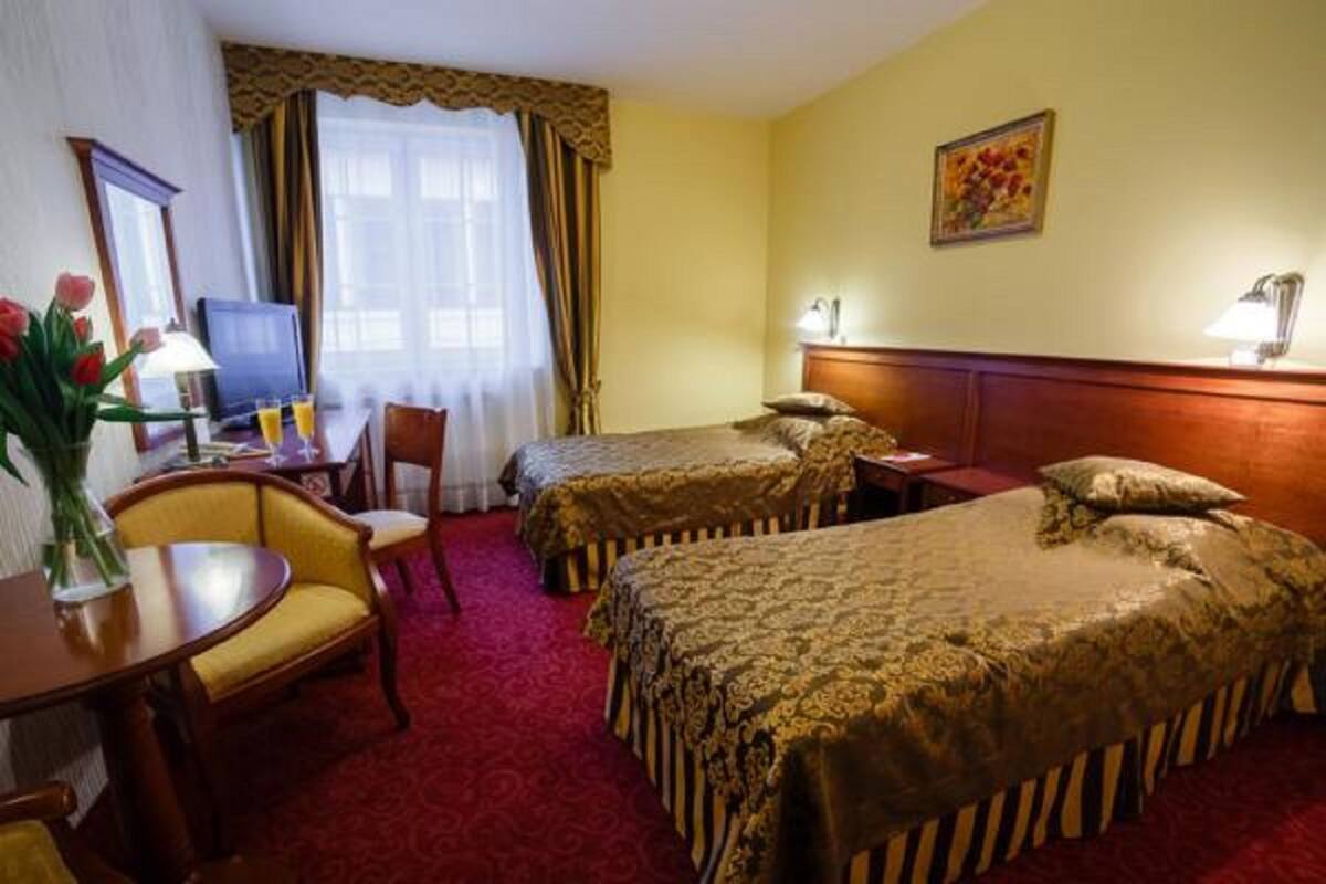 Habitación de hotel con dos camas, un escritorio con silla, televisión y un florero con flores.