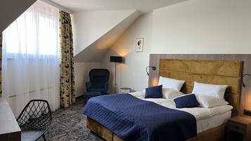 A hotel room with a large bed, a desk, a chair, and a window with curtains.