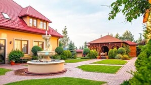 Um pátio com uma fonte, um gazebo e jardins bem cuidados.