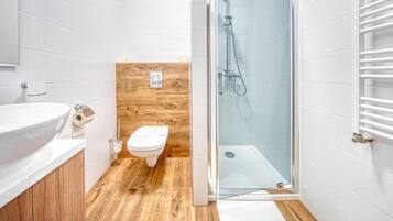Un baño moderno con lavamanos blanco, inodoro y ducha con cerramiento de vidrio.