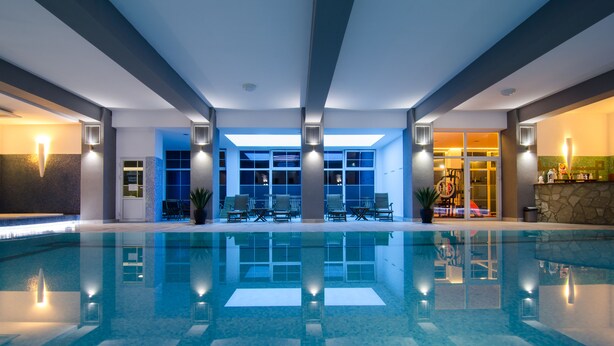 Piscina interior moderna com água cristalina, rodeada por espreguiçadeiras e uma área de recepção.