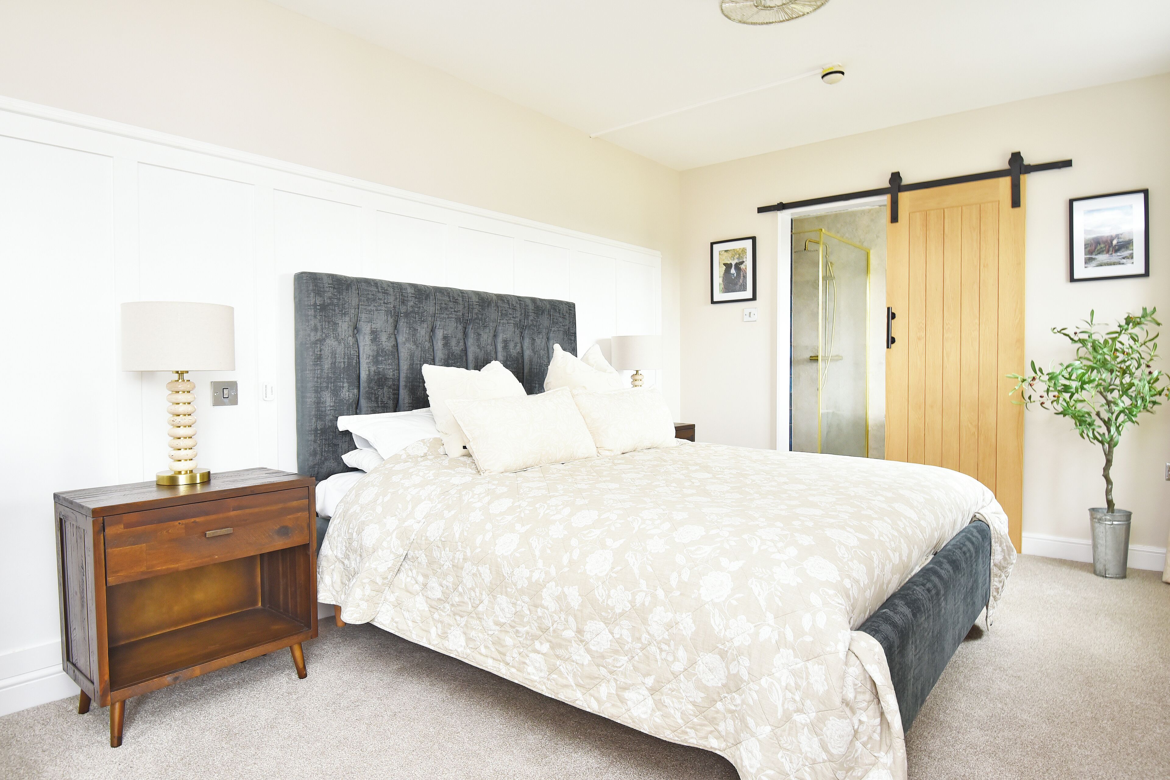 A bedroom with a bed, a nightstand, a lamp, a sliding door, and a potted plant.