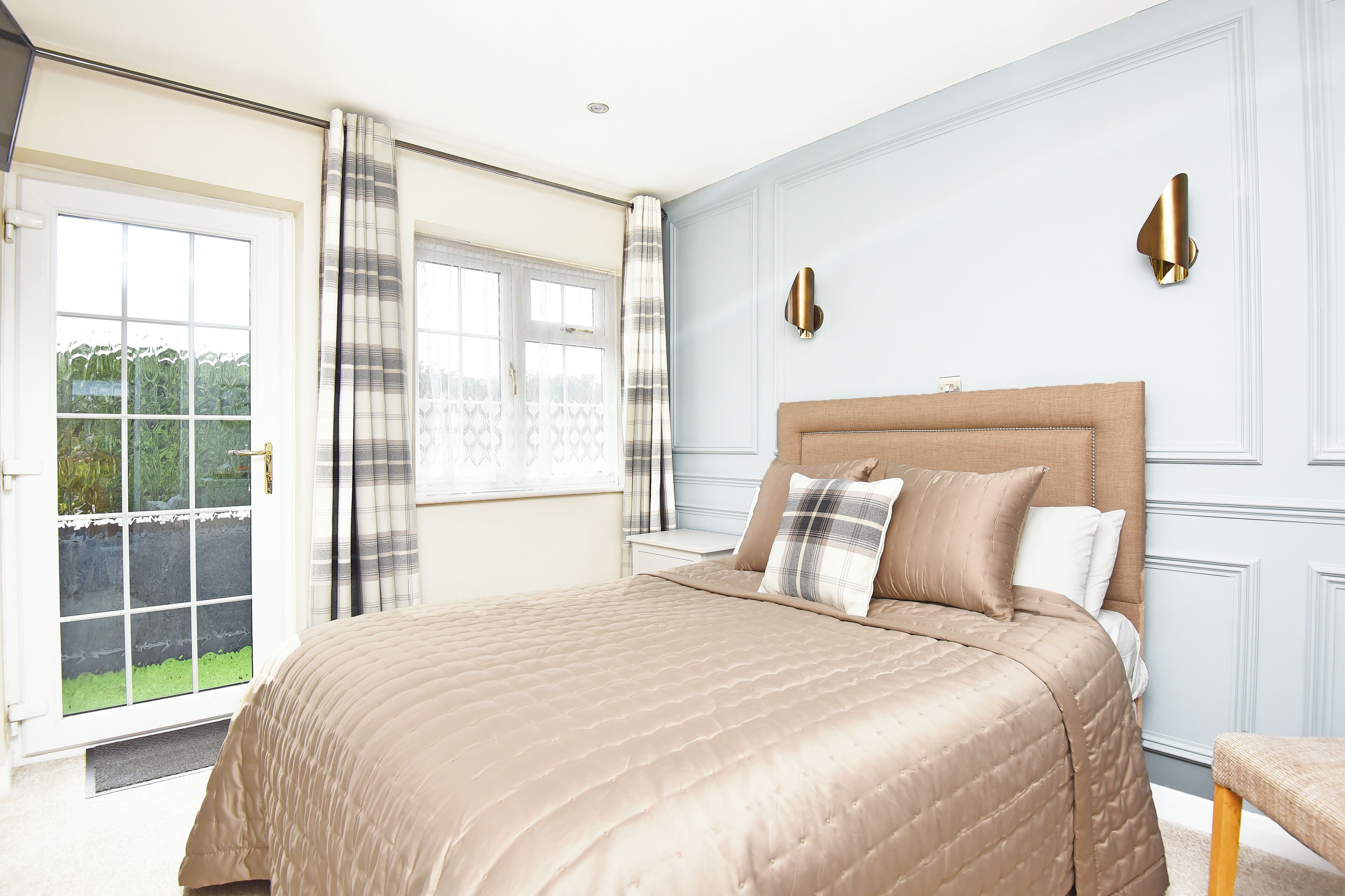 A bedroom with a large bed, a window with curtains, and a wall-mounted light fixture.