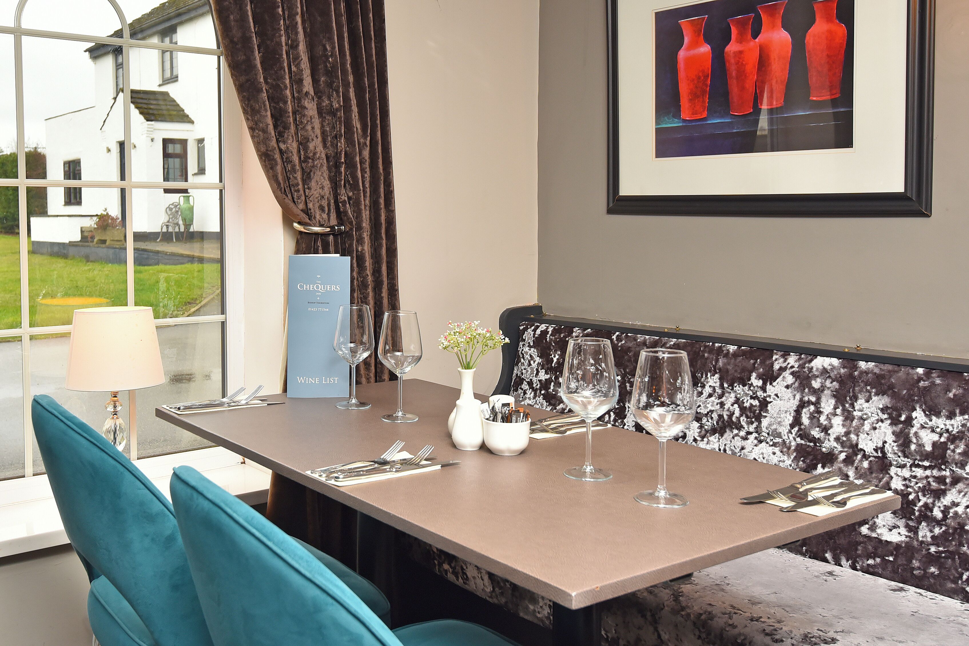 A dining table set with wine glasses, a vase with flowers, and a framed artwork of red vases.