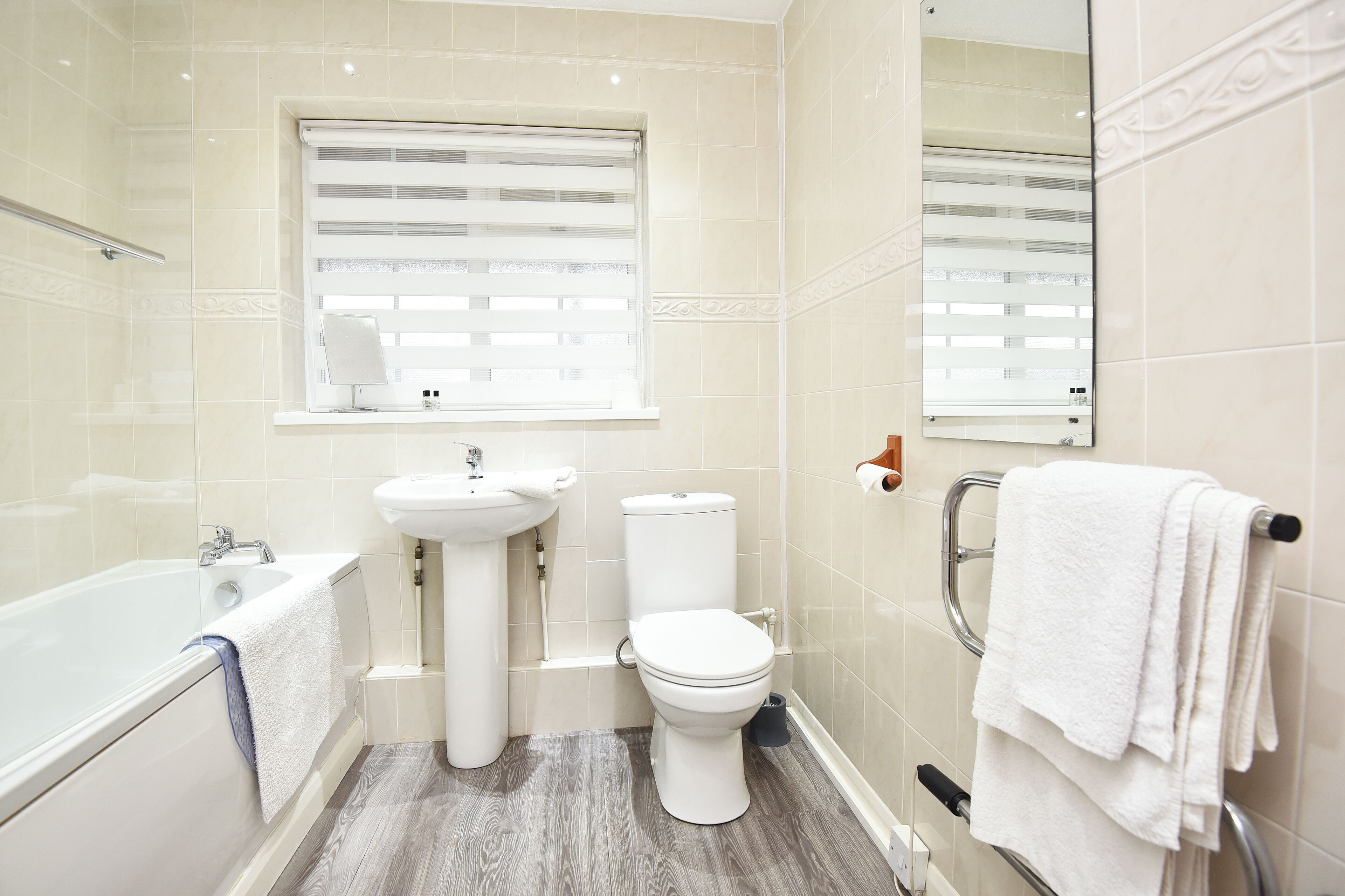A bathroom with a bathtub, toilet, sink, and a window with blinds.