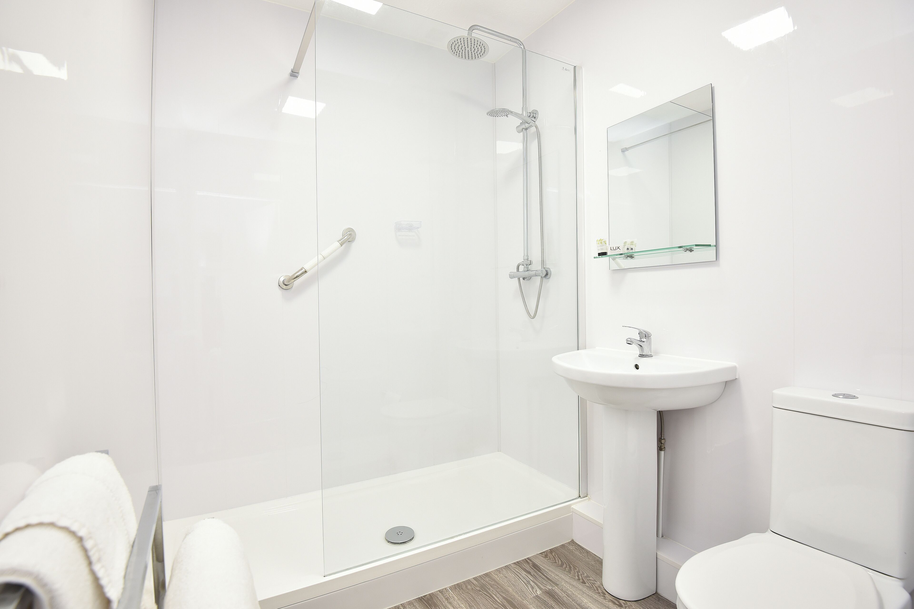 A modern bathroom with a glass-enclosed shower, a pedestal sink, and a toilet.