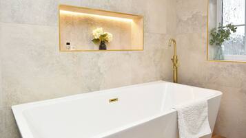 A modern bathroom with a freestanding bathtub, a wall-mounted mirror, and a window with a plant.