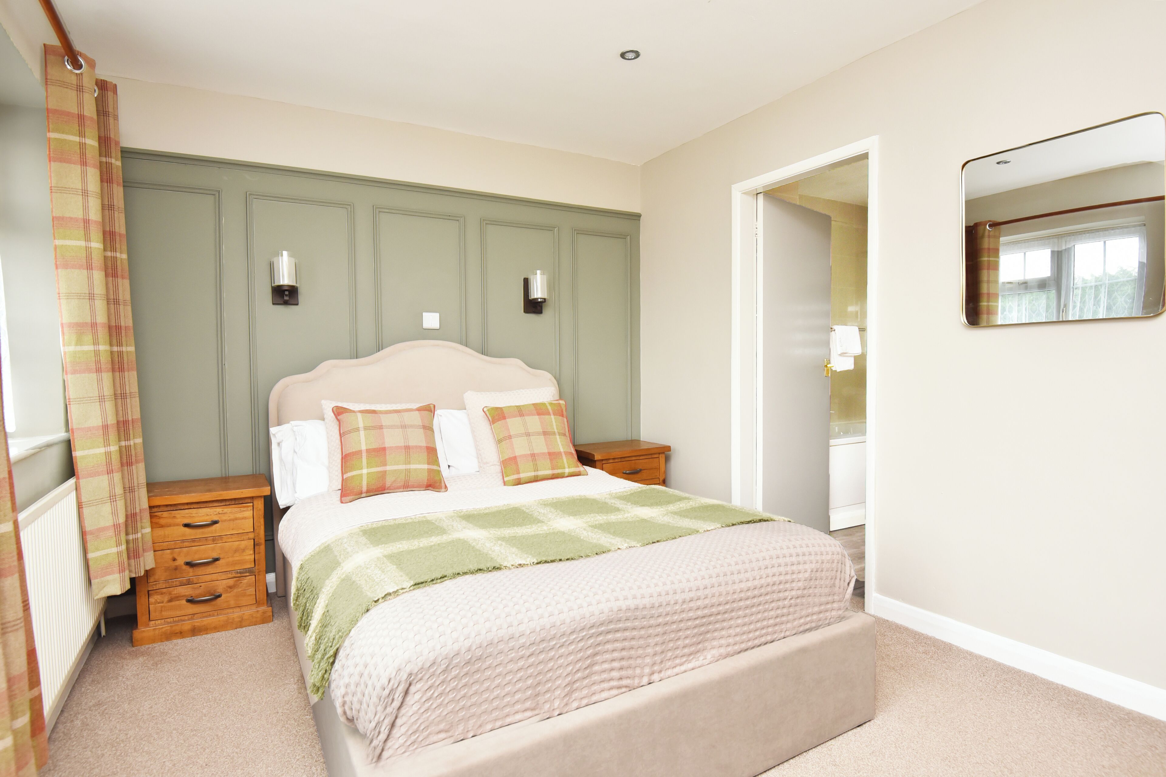 A bedroom with a bed, nightstands, a dresser, a mirror, and a door leading to another room.