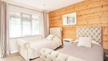 A bedroom with two beds, wooden paneling on the walls, a large window with curtains, and a mirror above the beds.