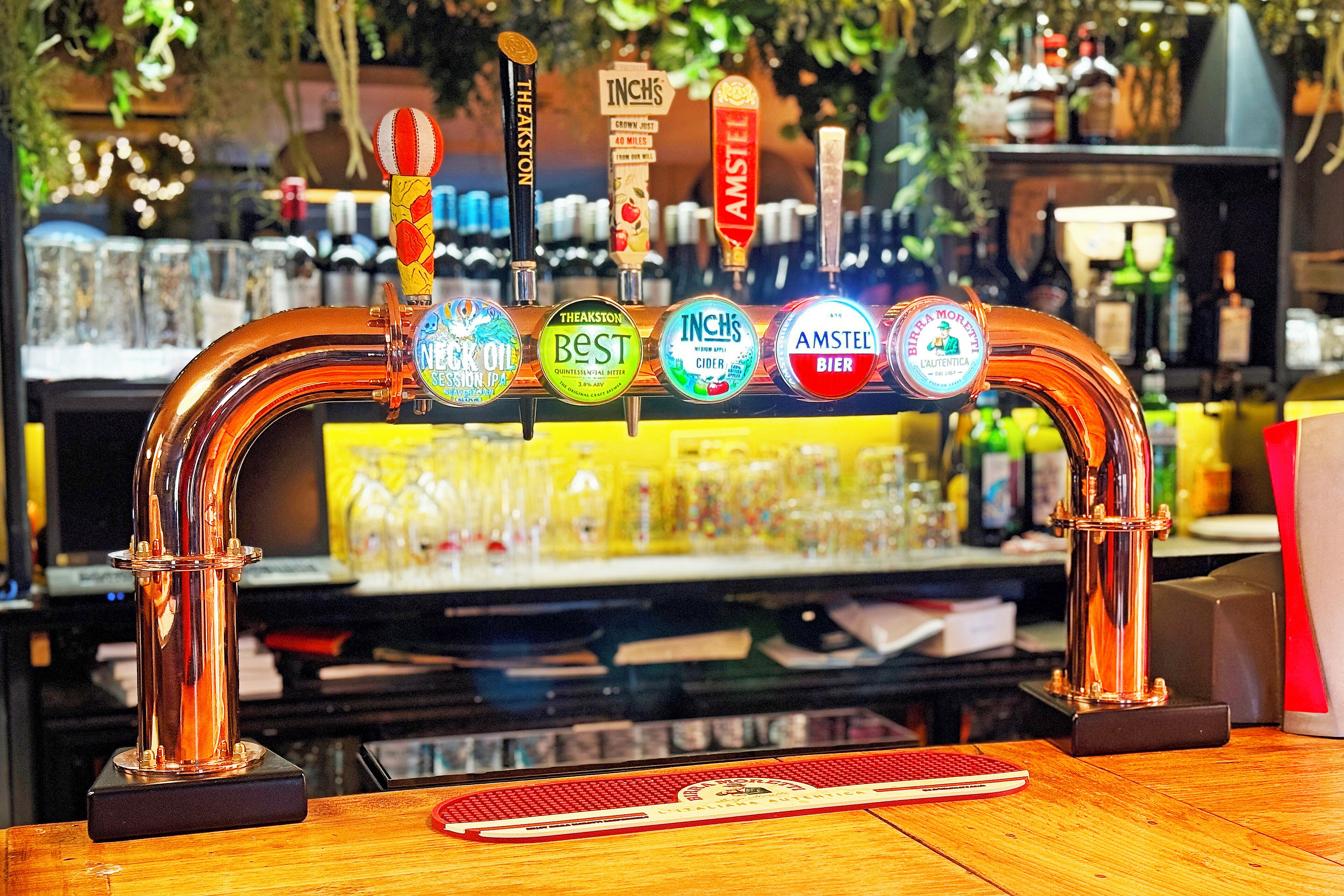 Een bar met kranen van koper, voorzien van labels met verschillende biermerken.