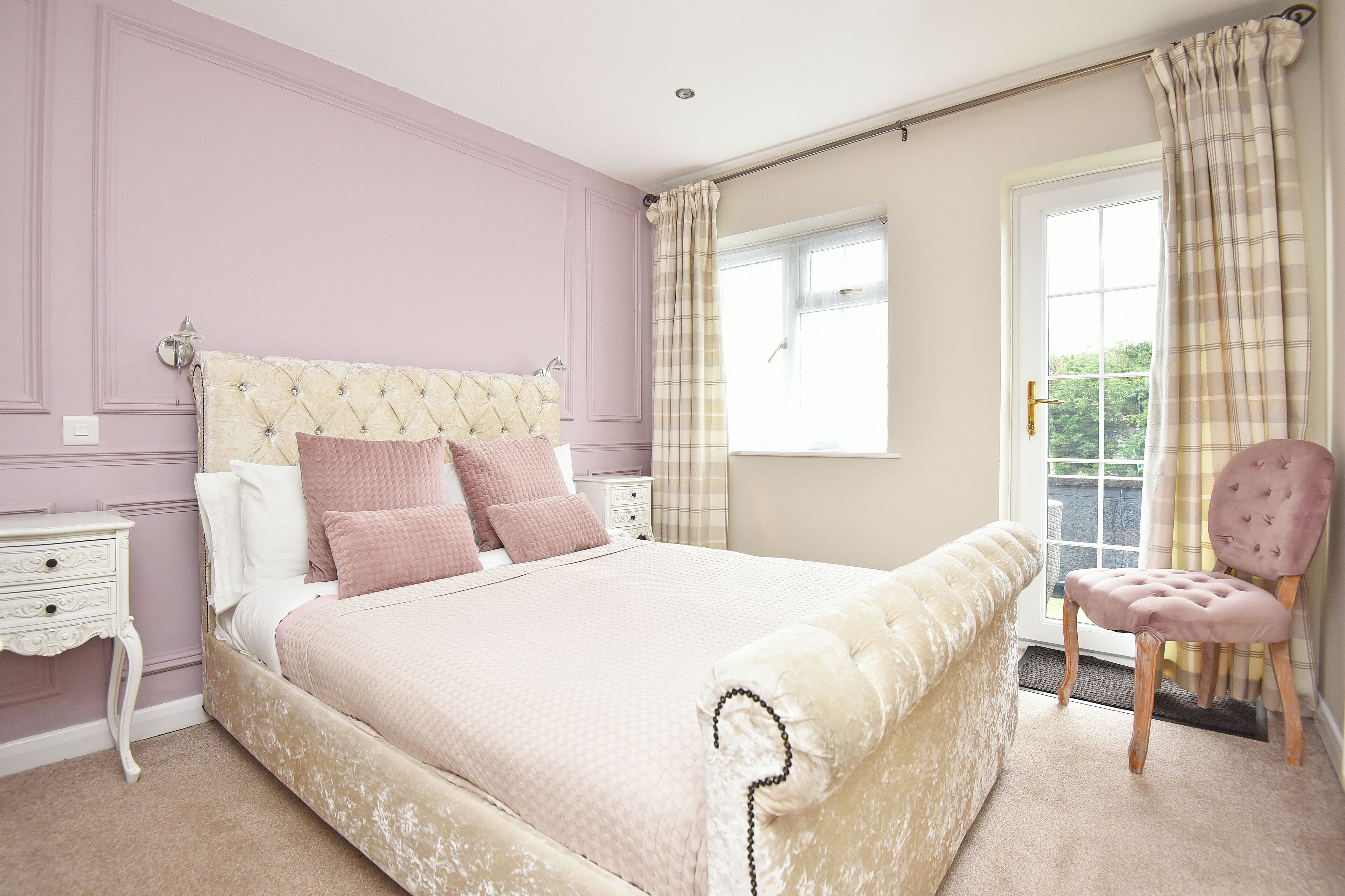 A bedroom with a large bed, a nightstand, a chair, and a window with curtains.