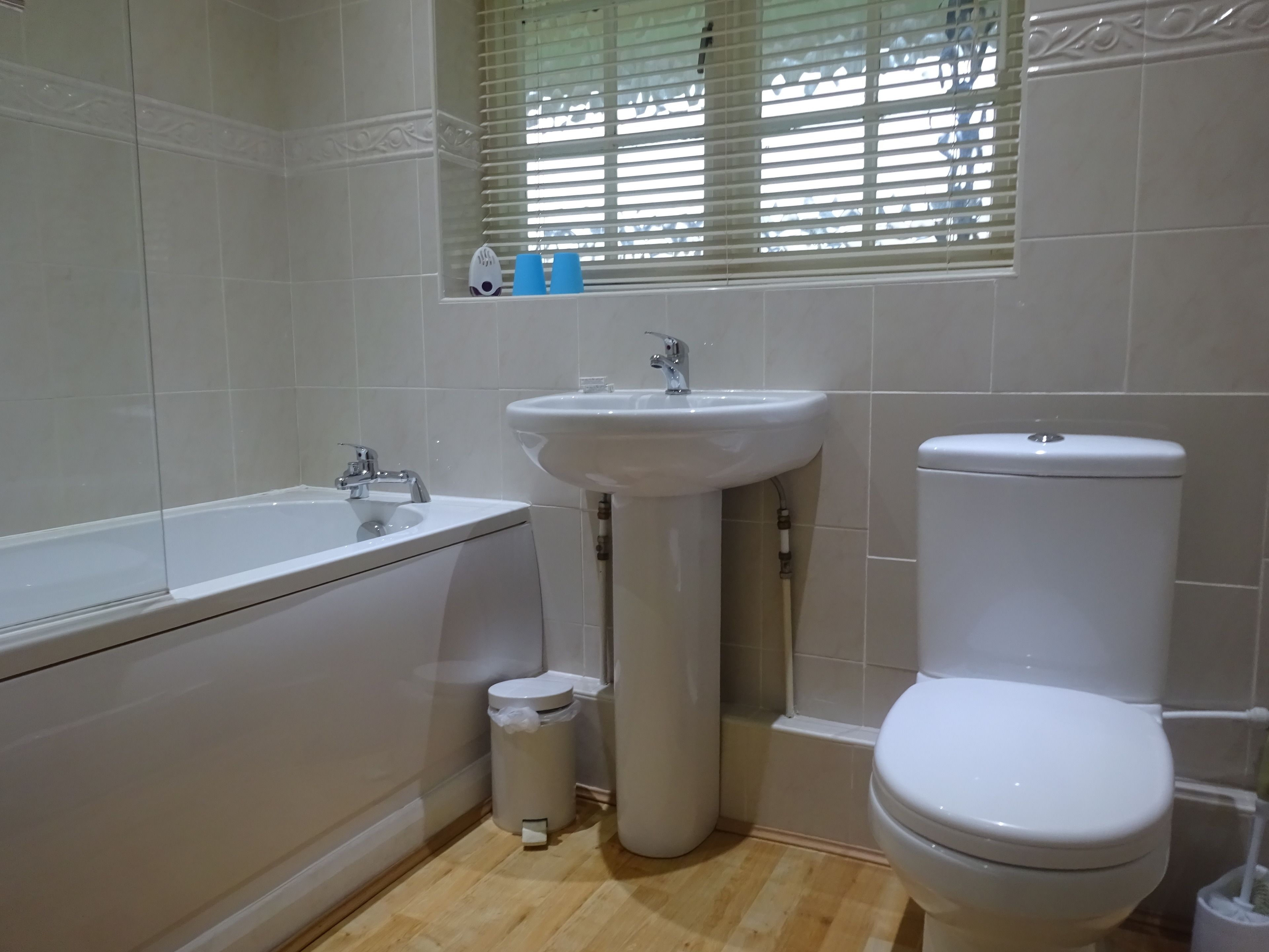 A bathroom with a bathtub, sink, toilet, and a window with blinds.