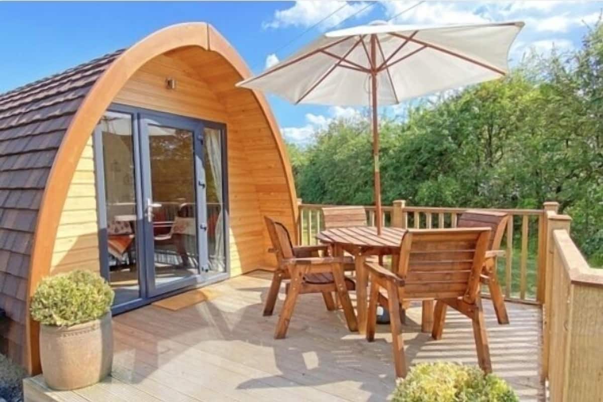 Une cabane en bois dotée d’une terrasse, de meubles de jardin et d’un grand parasol.