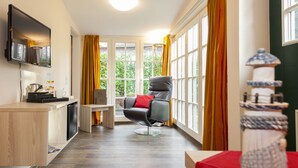 A modern room with a flat-screen TV, a massage chair, a small table, and a window with curtains.