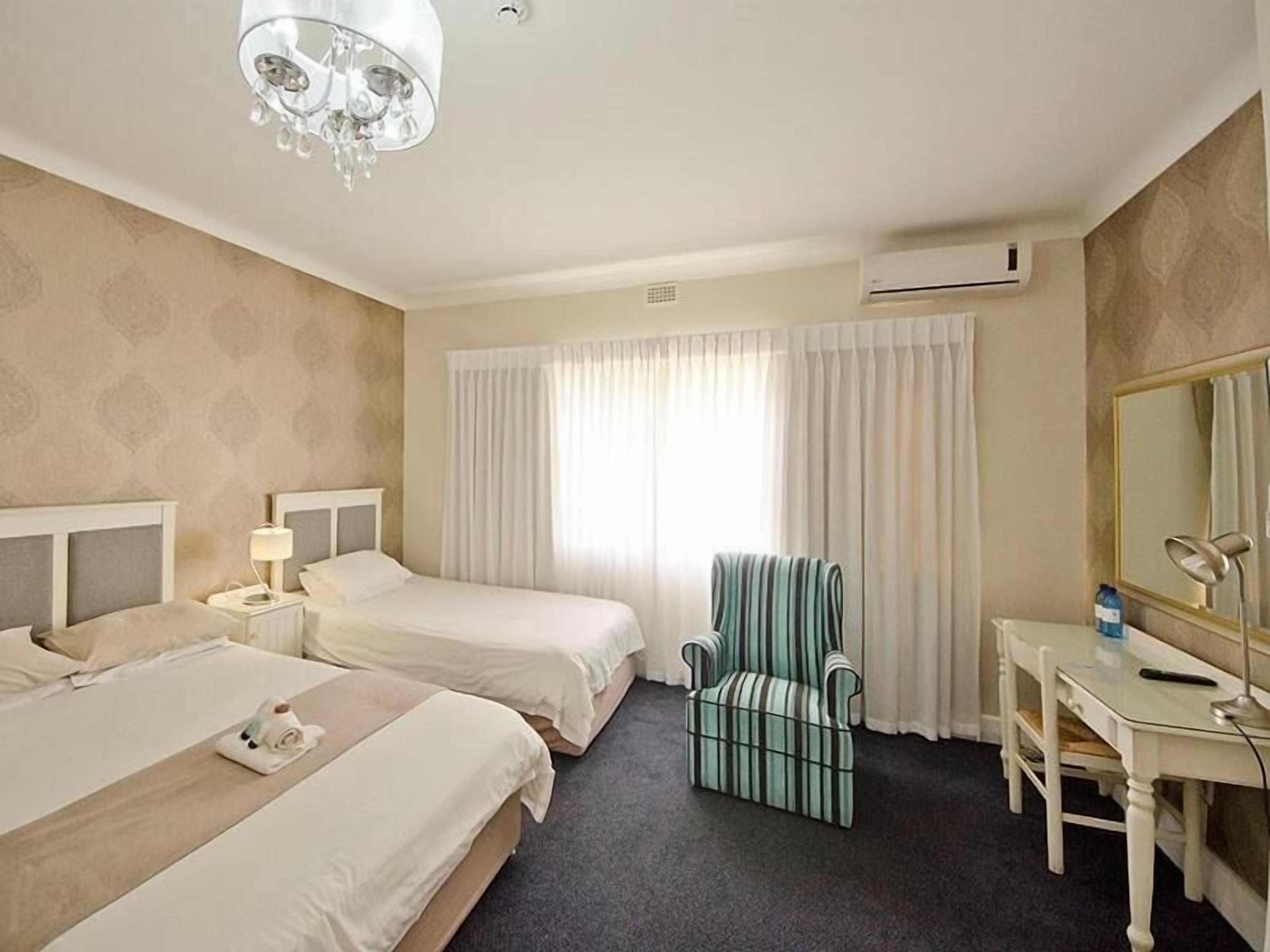 A hotel room with two beds, a desk, a chair, a chandelier, and an air conditioning unit.