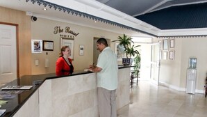 A hotel reception area with a marble counter, framed pictures on the wall, and a potted plant. - The Russel Hotel (Knysna)