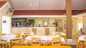 A restaurant with wooden chairs and tables, a counter with staff, and potted plants. - The Russel Hotel (Knysna)