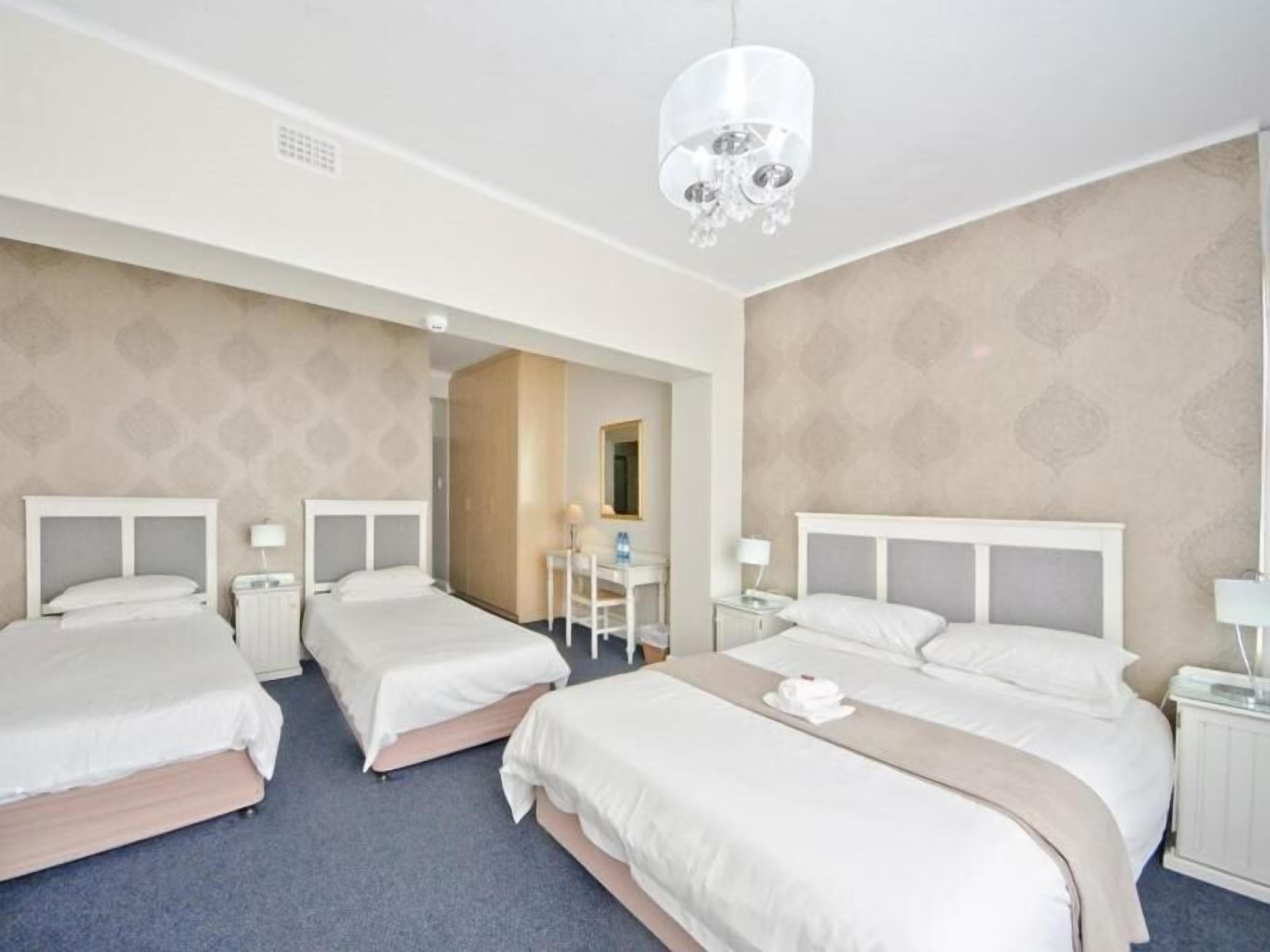 A hotel room with three beds, a desk, and a chandelier.