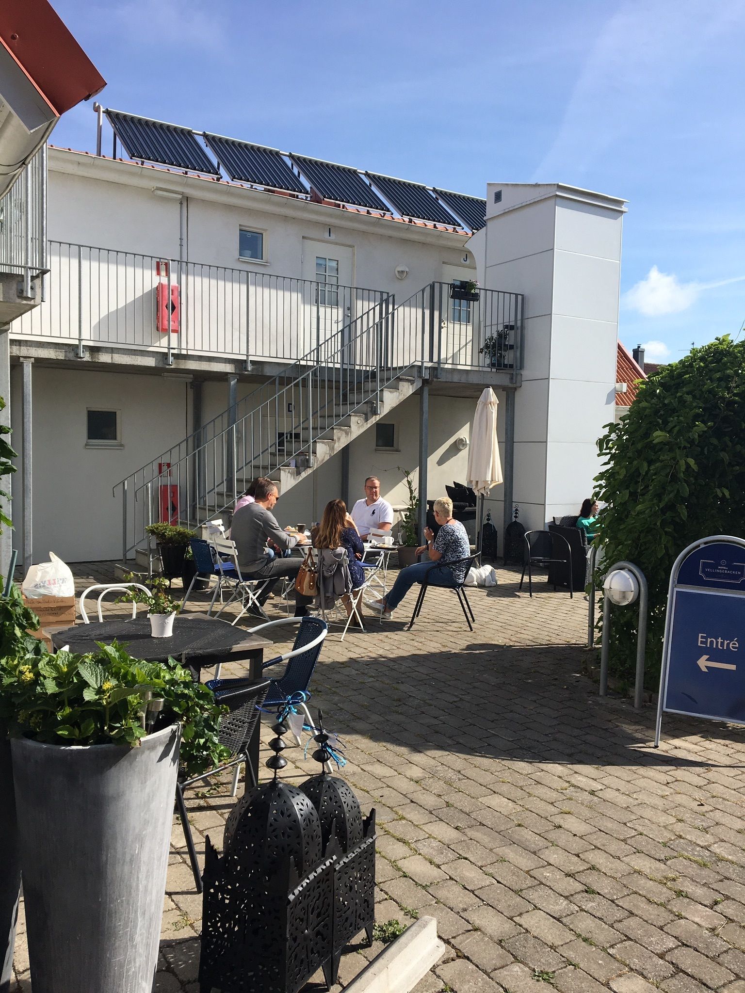 An outdoor café area with tables and chairs, a staircase, and a building with solar panels.