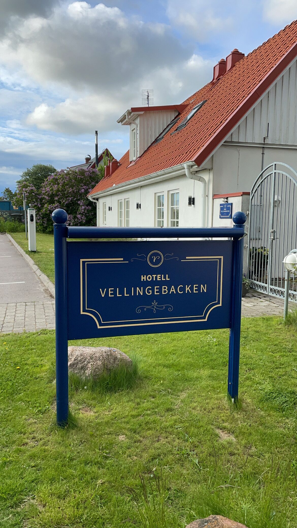 A hotel sign with the name "HOTELL VELLINGEBACKEN" and a traditional building with a red roof in the background.