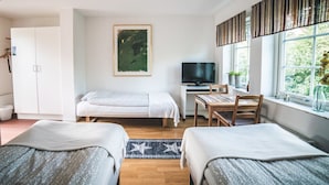 Un dormitorio con dos camas individuales, un escritorio con silla, un televisor y una ventana con vista a follaje.