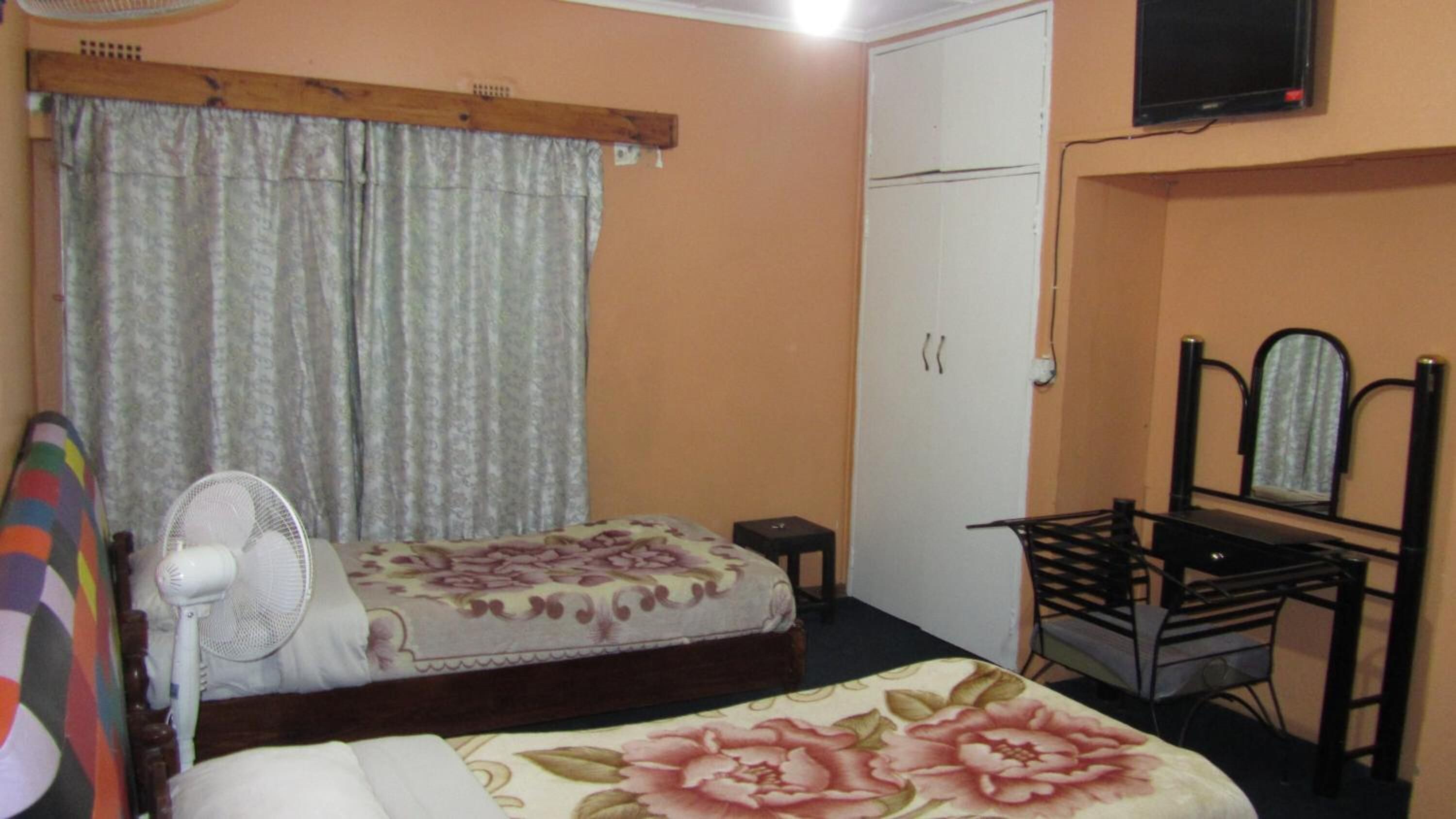 A bedroom with a bed, a chair, a desk, a mirror, and a television.