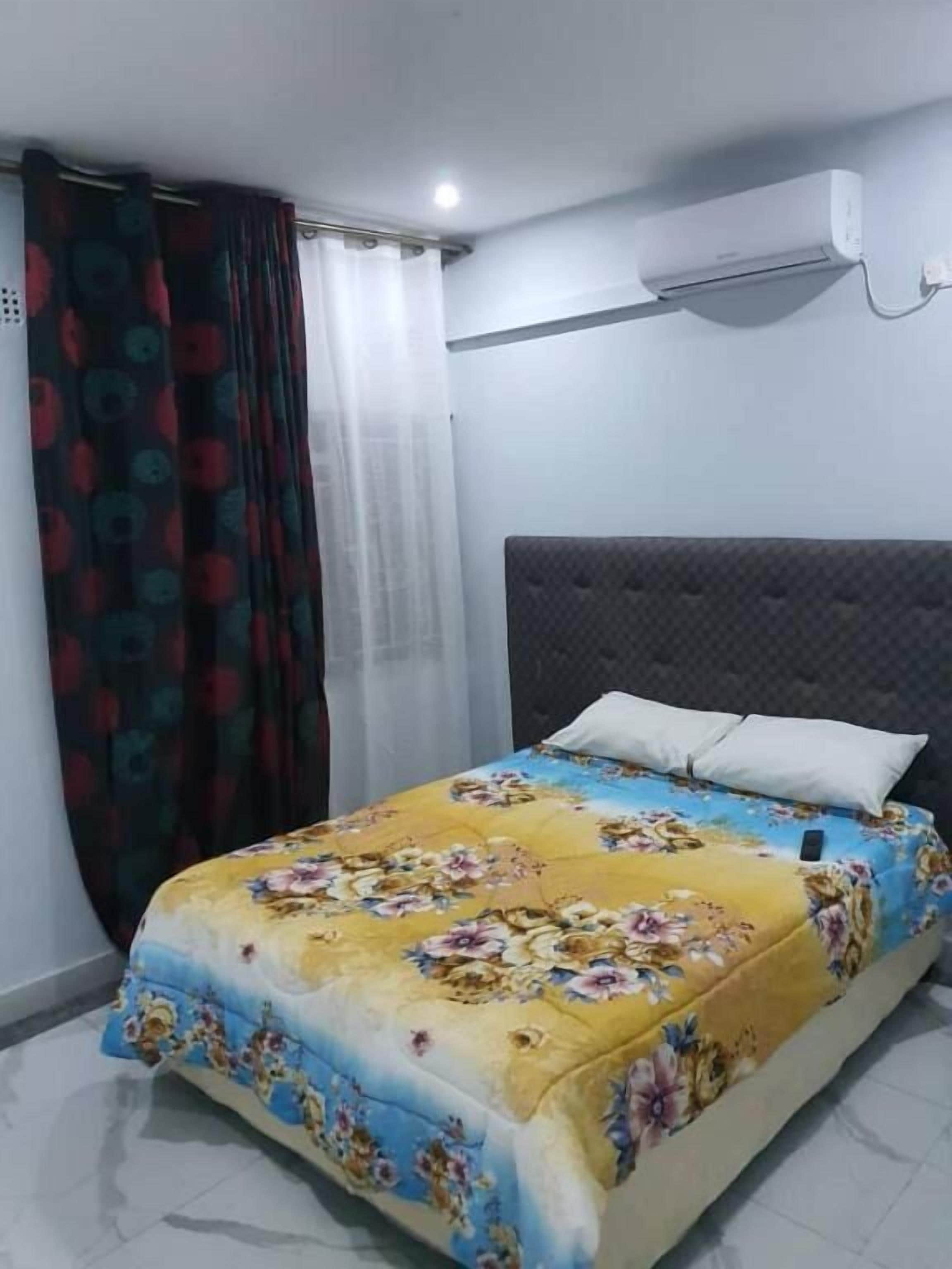 A bedroom with a bed, a headboard, a window with curtains, and an air conditioning unit.
