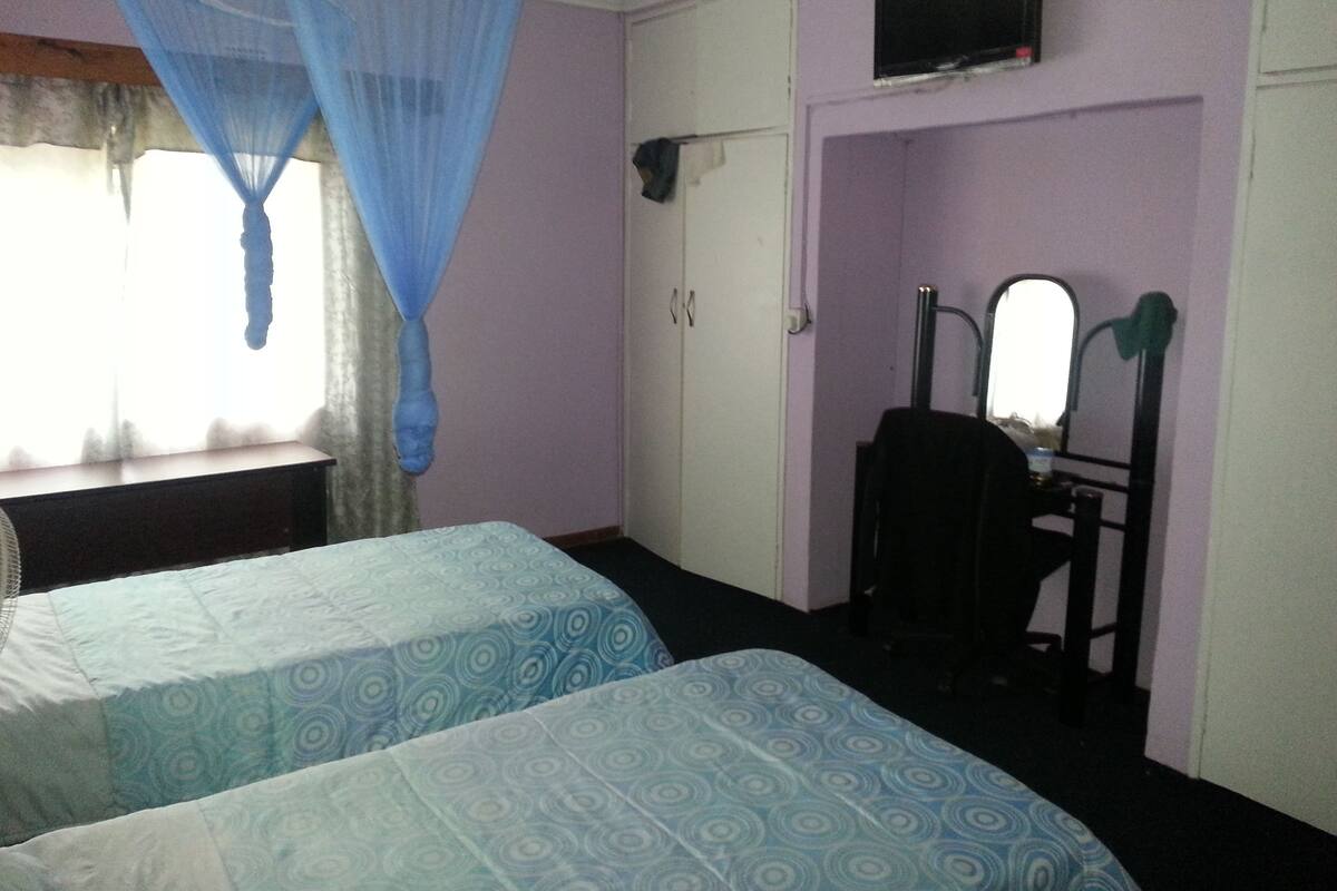 A room with two beds, a desk, a chair, a TV, and a wardrobe.