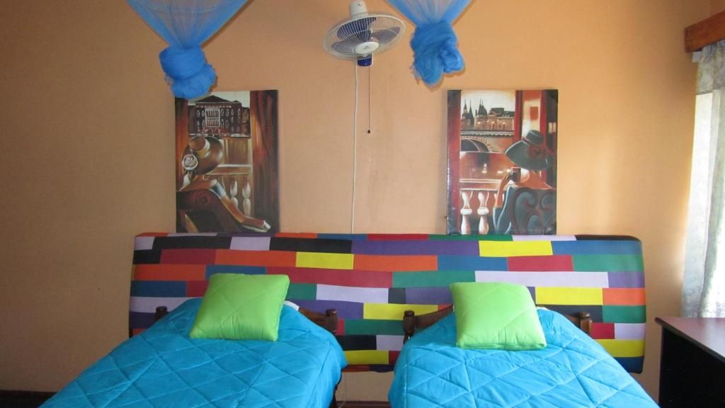 A room with two beds, a ceiling fan, and a colorful wall.