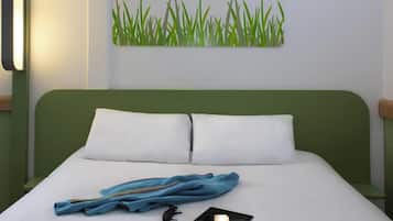 Una cama bien hecha con sábanas blancas y dos almohadas, una chaqueta azul, unas gafas de sol y una tablet sobre la cama.
