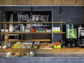 A breakfast buffet with various food items, coffee machines, and kitchenware.