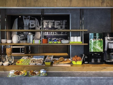 A breakfast buffet with various food items, coffee machines, and kitchenware.. ibis budget Chambéry Sud Challes les Eaux