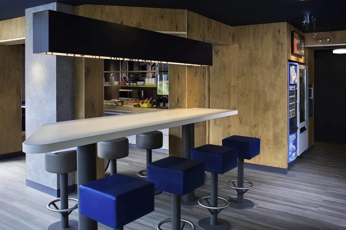 A modern bar area with a long counter, four blue bar stools, and a vending machine.