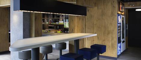 A modern bar area with a long counter, four blue bar stools, and a vending machine.