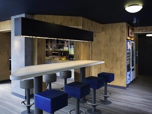 Eine moderne Bar mit einer langen Theke, vier blauen Barhocker und einem Automaten.